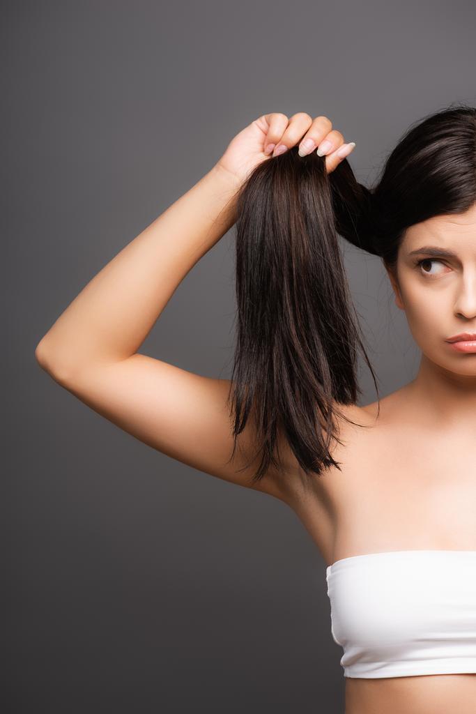 cropped view of upset brunette woman holding damaged hair isolated on black - Photo, Image