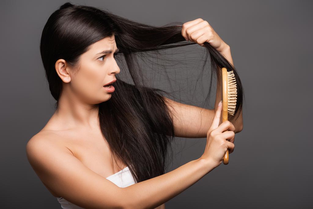 järkyttynyt brunette nainen harjaamalla hiukset eristetty musta - Valokuva, kuva
