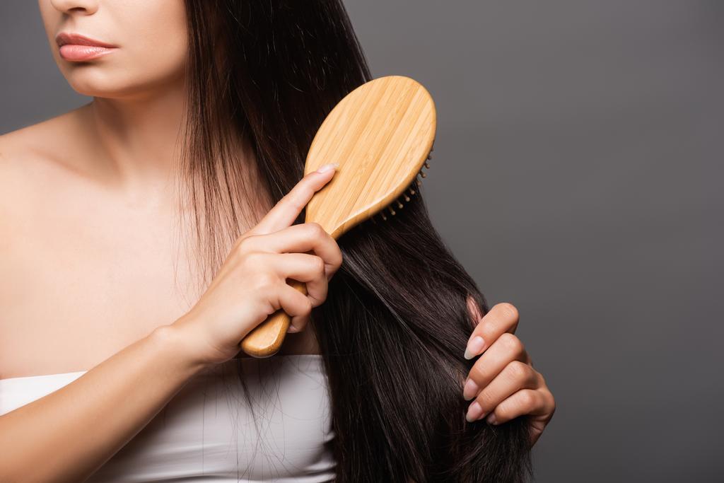ostříhaný pohled na bruneta žena kartáčování vlasy izolované na černé - Fotografie, Obrázek