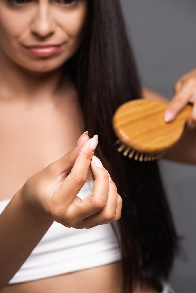 selective focus of brunette woman holding lost hair while brushing isolated on black - Photo, Image