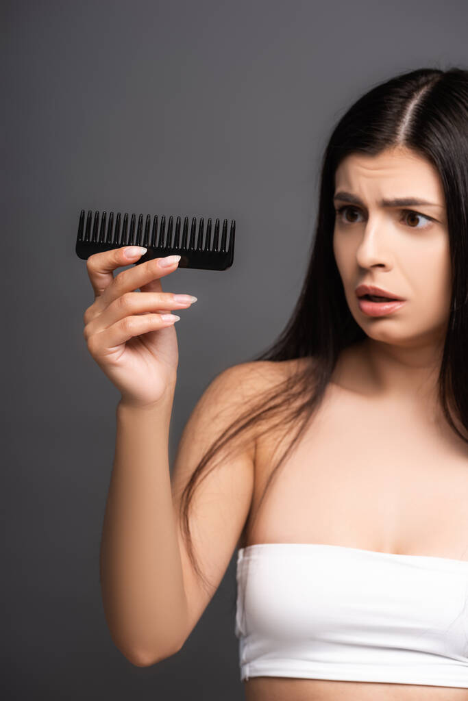 shocked brunette woman looking at comb isolated on black - Photo, Image