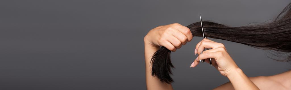 обрізаний вид на голу брюнетку, що ріже волосся ізольовано на чорному, панорамний знімок
 - Фото, зображення