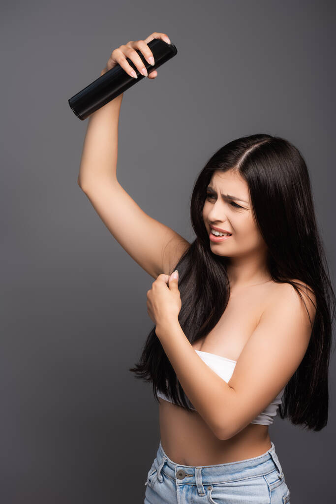 morena de cabelos longos mulher aplicando spray de cabelo com olhos fechados isolados em preto - Foto, Imagem