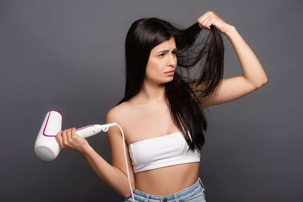 upset brunette long haired woman with hair dryer isolated on black - Photo, Image