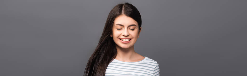 brunette langharige vrouw met gesloten ogen glimlachen geïsoleerd op zwart, panoramisch schot - Foto, afbeelding