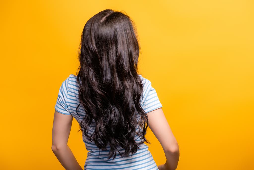 vue arrière du vent soufflant à travers les cheveux bruns de la femme avec des boucles isolées sur jaune - Photo, image