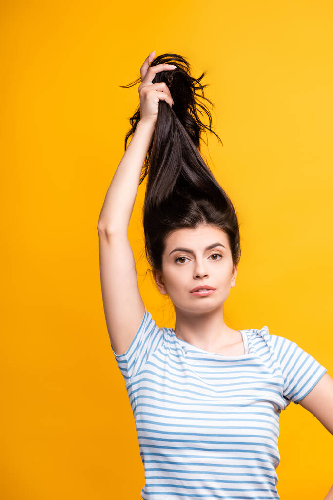 brunette woman holding hair above head isolated on yellow - Photo, Image