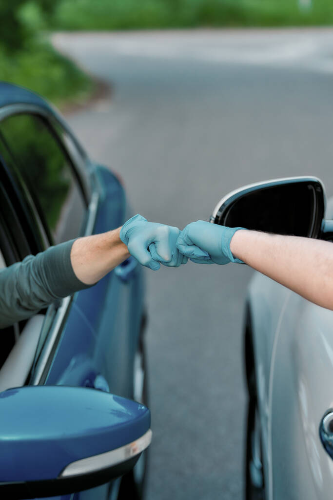 Primo piano delle mani di due automobilisti che indossano guanti protettivi, facendo urtare il pugno mentre si salutano sulla strada - Foto, immagini