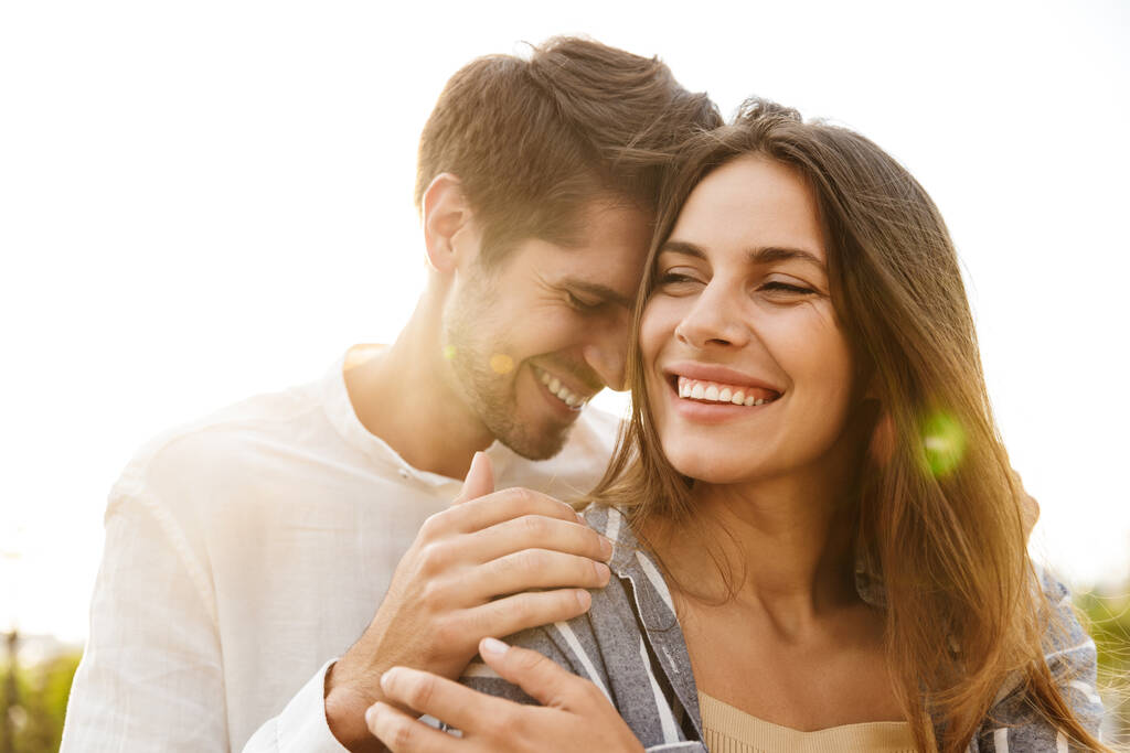 Imagem de jovem casal feliz caucasiano sorrindo e abraçando enquanto caminhava ao ar livre - Foto, Imagem