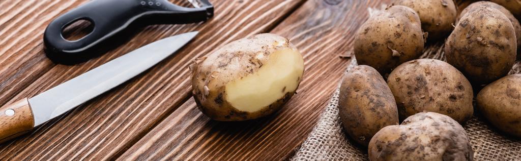 schmutzige Kartoffeln auf Holztisch mit Schäler und Messer, Panoramaaufnahme - Foto, Bild