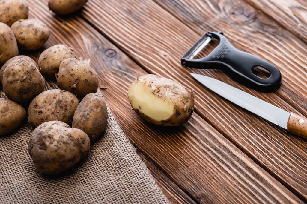 брудна картопля на дерев'яному столі з шкіркою і ножем
 - Фото, зображення