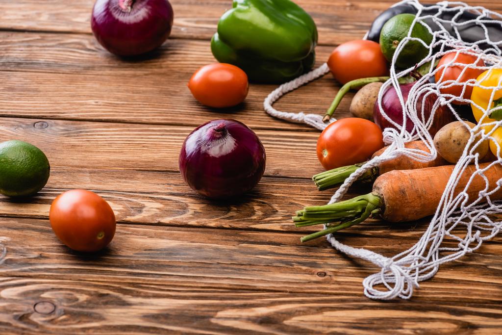 légumes frais mûrs éparpillés dans un sac à ficelle sur une table en bois - Photo, image
