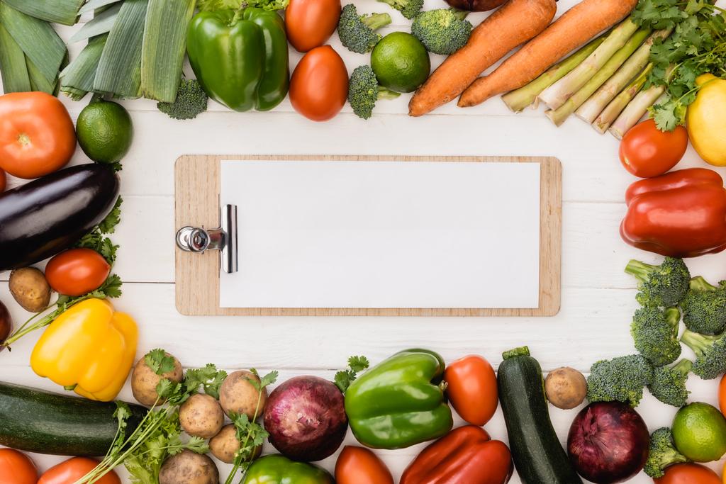 vista superior de verduras frescas maduras y frutas cerca del portapapeles vacío sobre fondo blanco de madera - Foto, Imagen