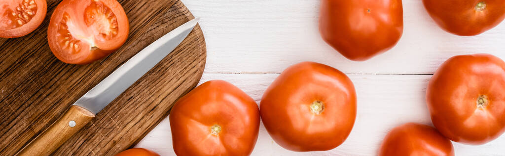 Draufsicht auf reife Tomaten auf Schneidebrett mit Messer auf weißem Holztisch, Panoramaaufnahme - Foto, Bild