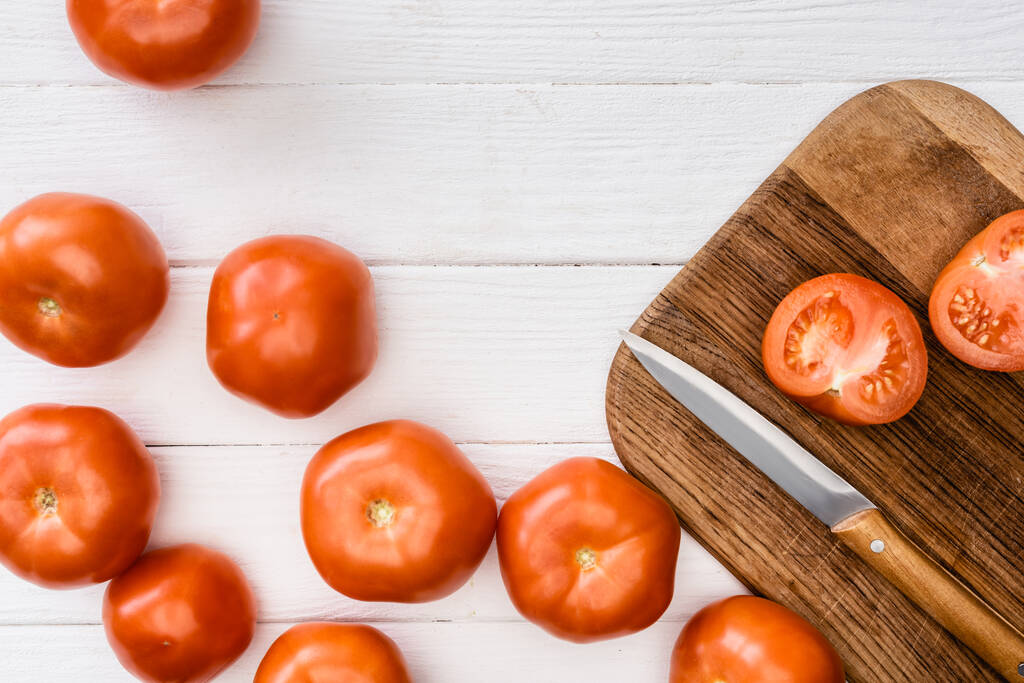 vista superior de tomates maduros sobre tabla de cortar con cuchillo sobre mesa de madera blanca - Foto, Imagen
