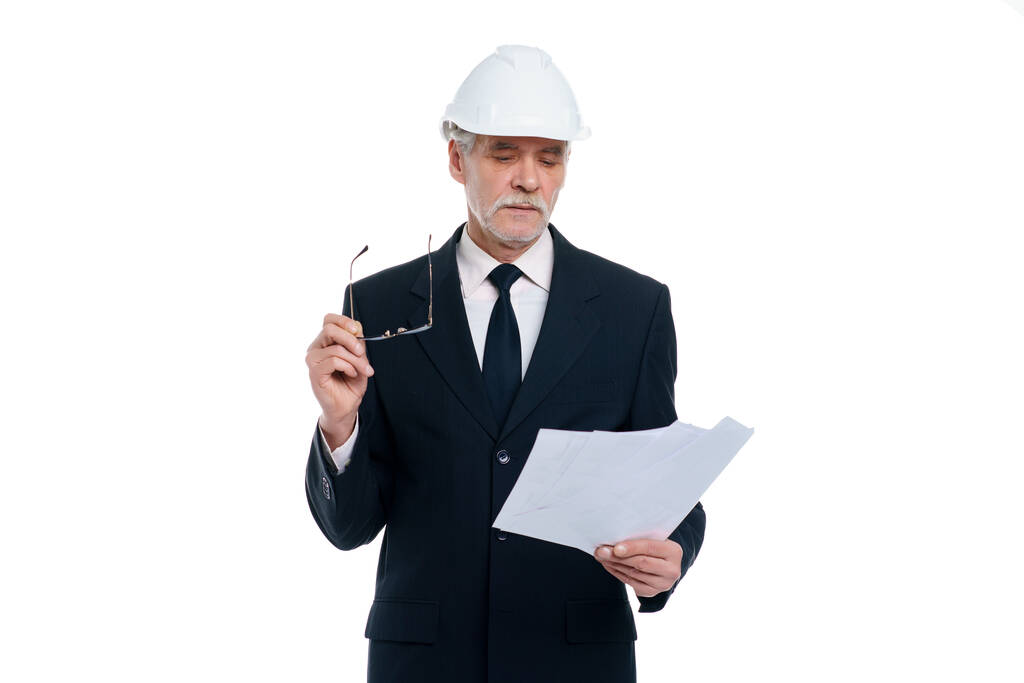 Старший бізнесмен, інженер-будівельник носить білий шолом безпеки з папером проекту ізольовано на білому тлі
. - Фото, зображення