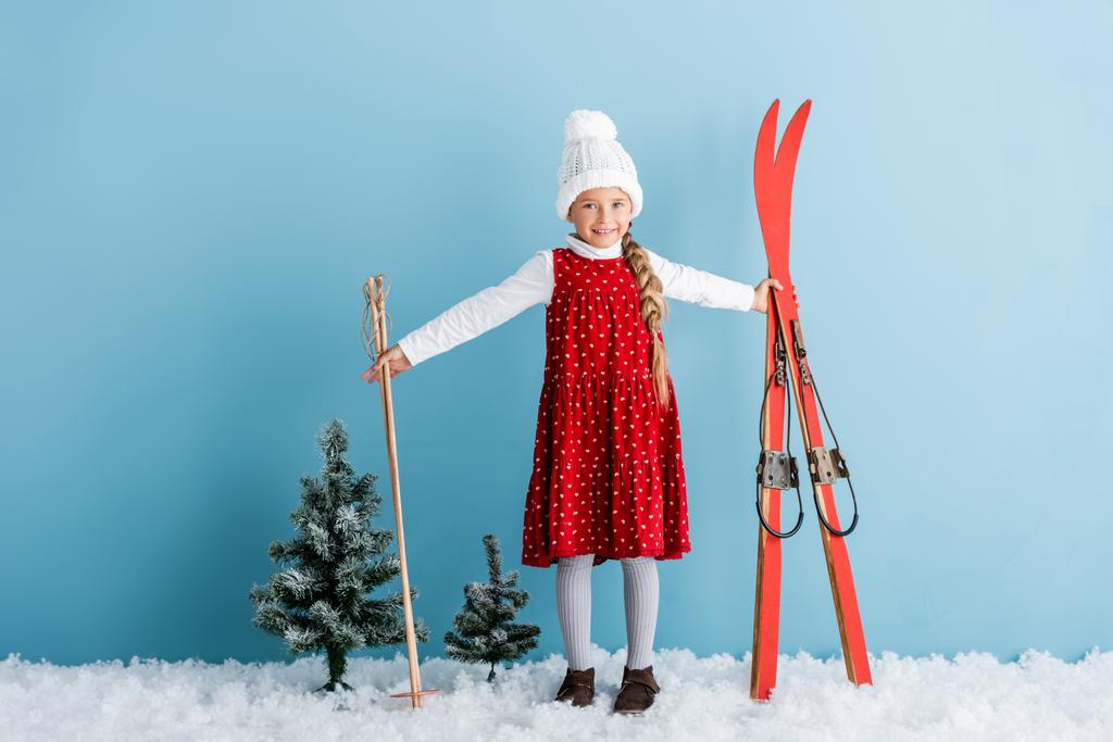 child in winter outfit standing on snow with ski poles and skis on blue - Photo, Image