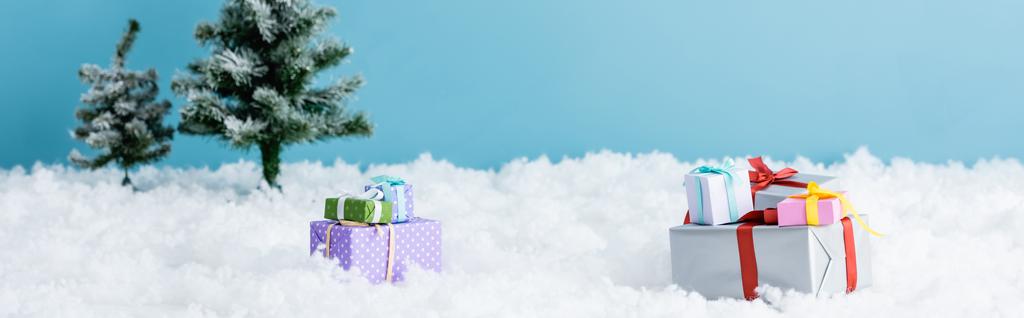 青い上に孤立したクリスマスツリーの近くの白い雪の上のプレゼントの水平画像  - 写真・画像