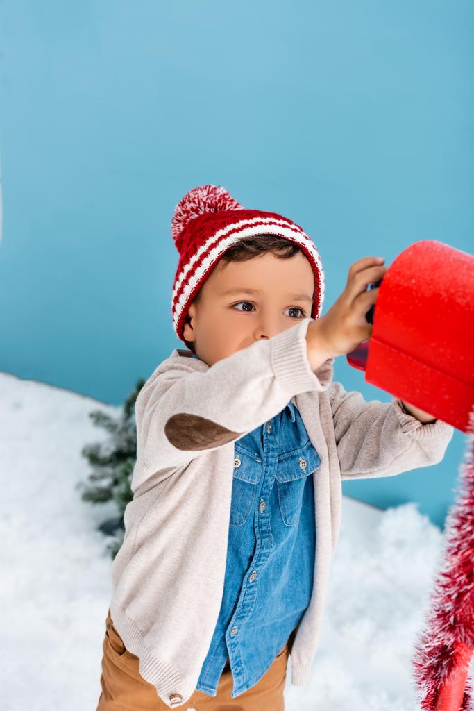 menino em roupa de inverno atingindo caixa de correio vermelho no azul  - Foto, Imagem
