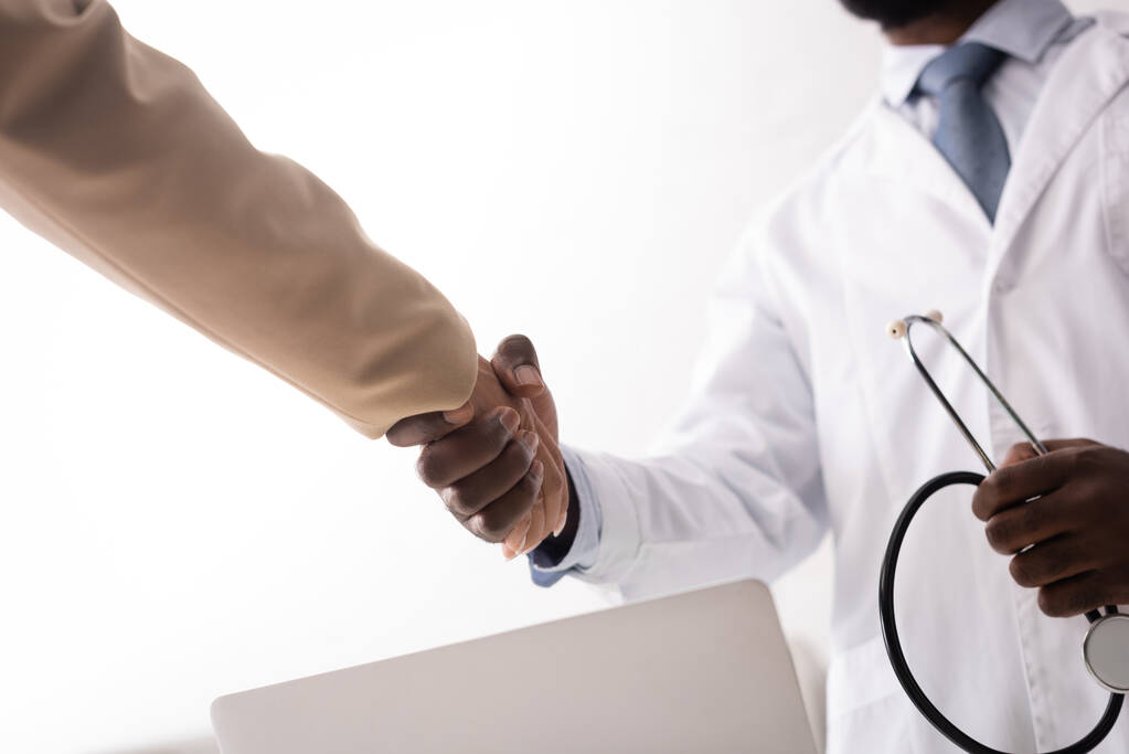 Enfoque selectivo del médico afroamericano sosteniendo estetoscopio y estrechando la mano con el paciente - Foto, imagen