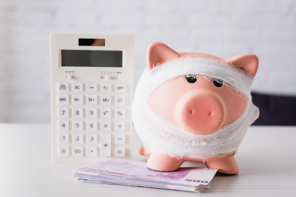 Foco selectivo do banco porquinho perto das notas de euro e calculadora na tabela branca - Foto, Imagem