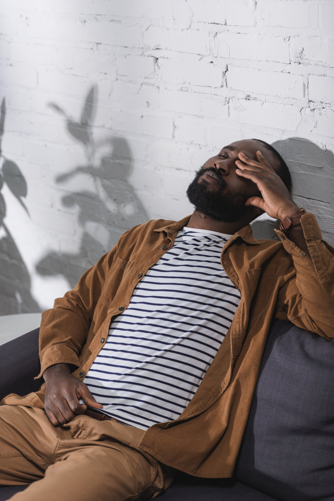 Αφροαμερικάνος κάθεται στον καναπέ με κλειστά μάτια - Φωτογραφία, εικόνα