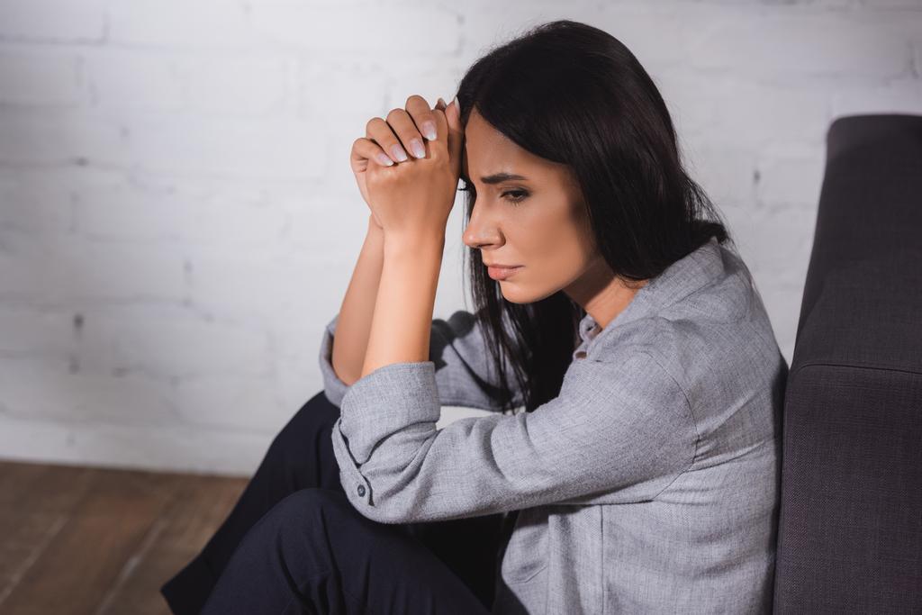 mujer estresada sosteniendo las manos apretadas cerca de la cabeza mientras está sentada en casa, concepto de salud mental - Foto, Imagen