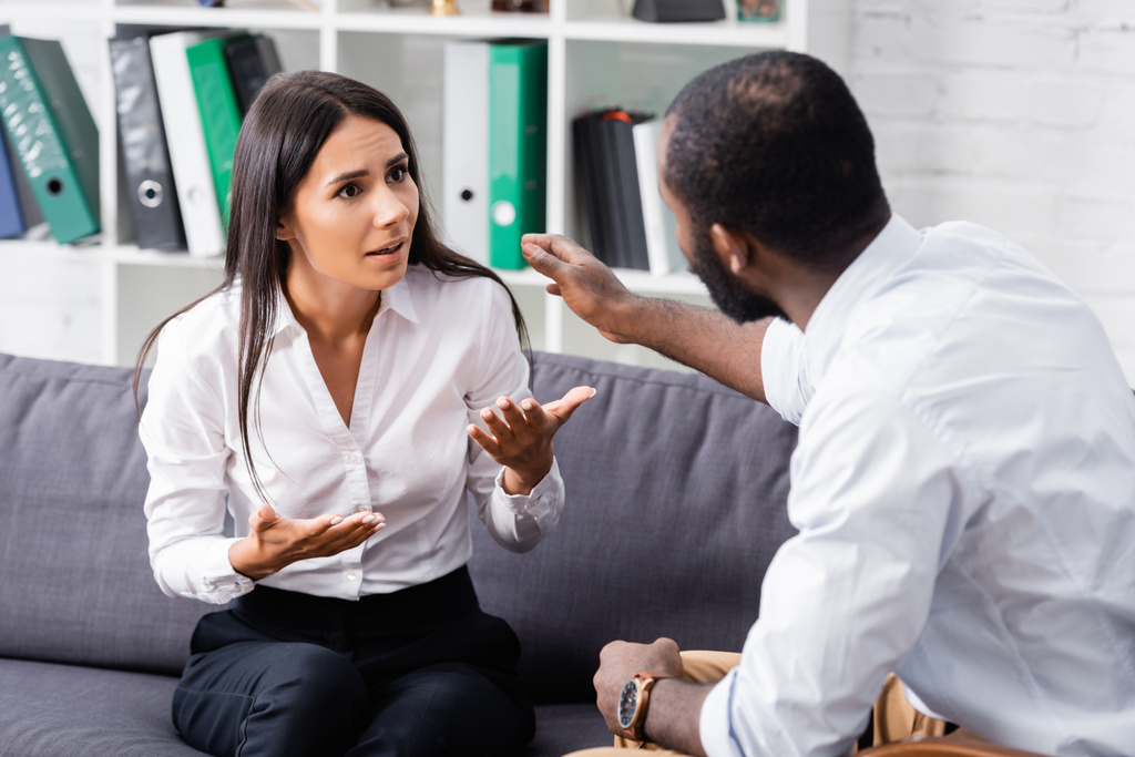 selective focus of african american psychologist calming frustrated patient talking and gesturing while sitting on sofa - Photo, Image