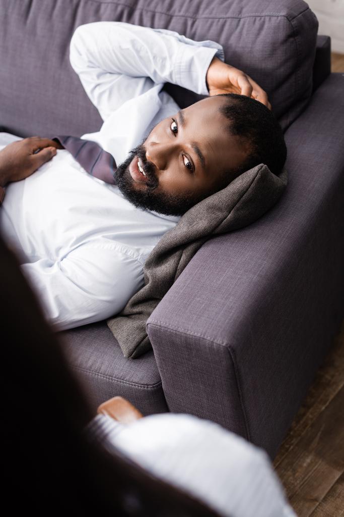 アフリカ系アメリカ人の患者がソファに寝そべって心理学者の近くで - 写真・画像