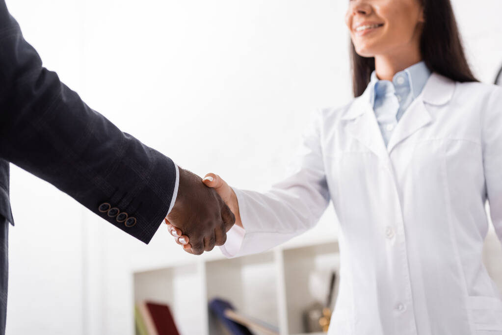 Ausgeschnittene Ansicht eines Arztes im weißen Kittel beim Händeschütteln mit einem afrikanisch-amerikanischen Patienten - Foto, Bild