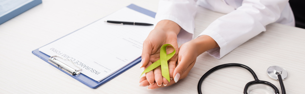 cropped view of doctor holding green awareness ribbon near stethoscope and insurance claim form, mental health concept, horizontal image - Photo, Image