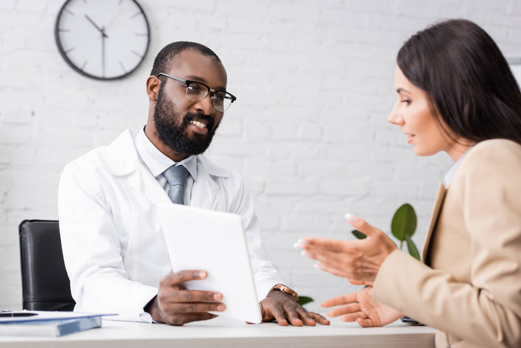 Gözlüklü Afrikalı Amerikalı doktorun seçici odak noktası dijital tableti hastayla konuşurken gösteriyor. - Fotoğraf, Görsel