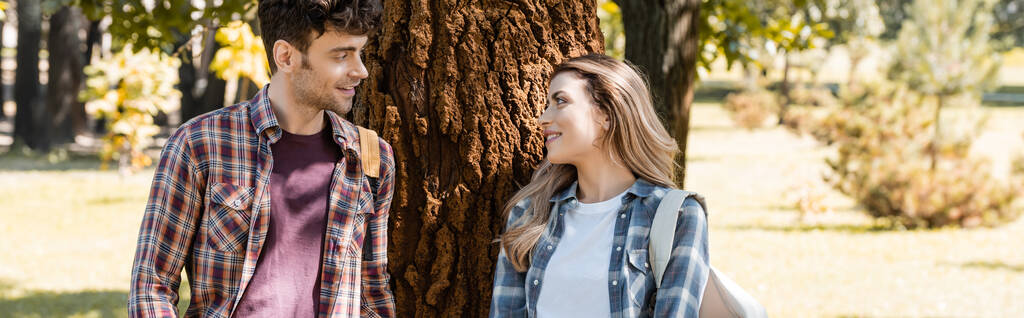 concepto panorámico de hombre y mujer mirándose el uno al otro cerca del tronco del árbol  - Foto, imagen