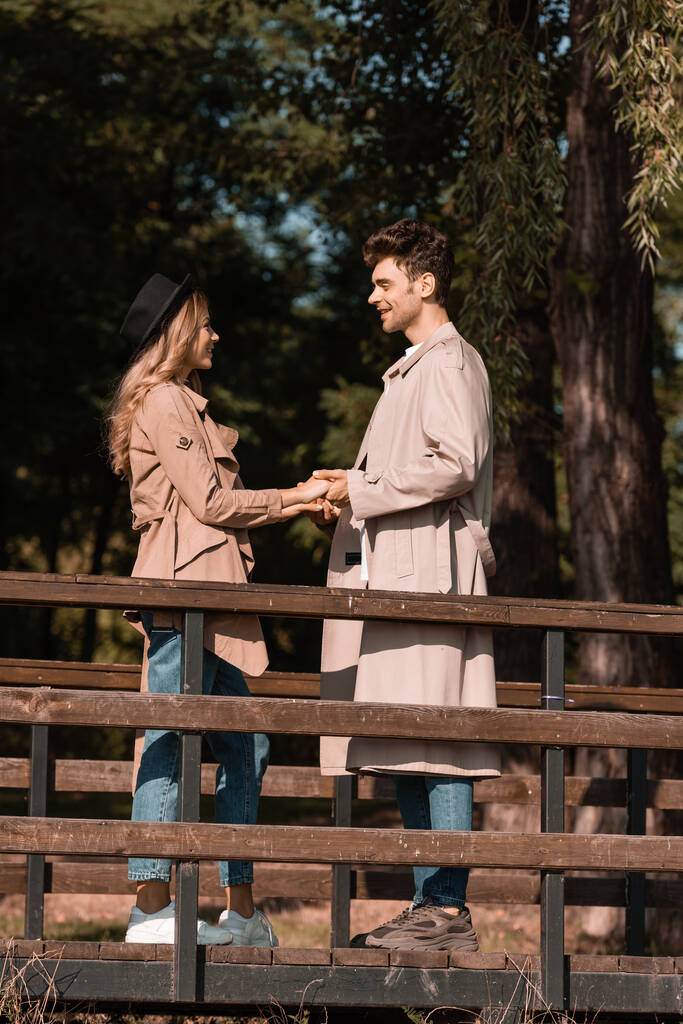 profil de couple élégant en trench manteaux tenant la main sur un pont en bois - Photo, image