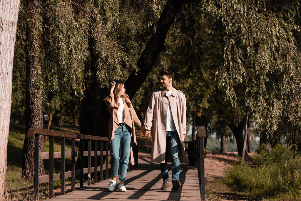 donna toccando cappello di paglia e guardando il fidanzato mentre cammina su un ponte di legno  - Foto, immagini