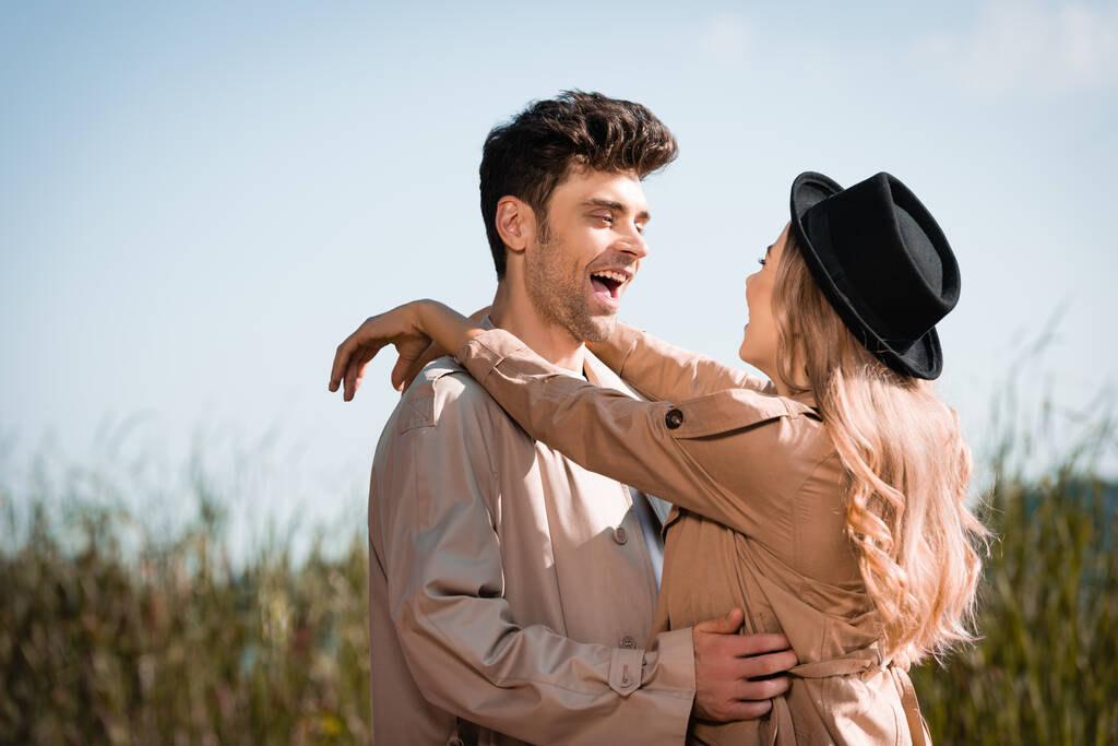 blonde woman in hat hugging excited man in trench coat  - Photo, Image