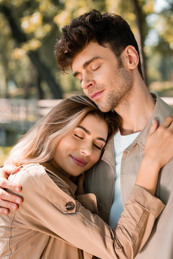novia abrazando novio con los ojos cerrados en el parque otoñal  - Foto, imagen