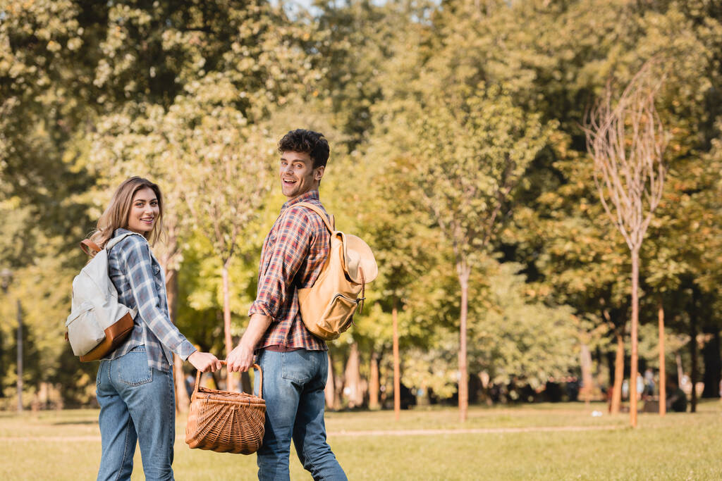 uomo con cesto di vimini che si tiene per mano con la donna mentre in piedi nel parco  - Foto, immagini
