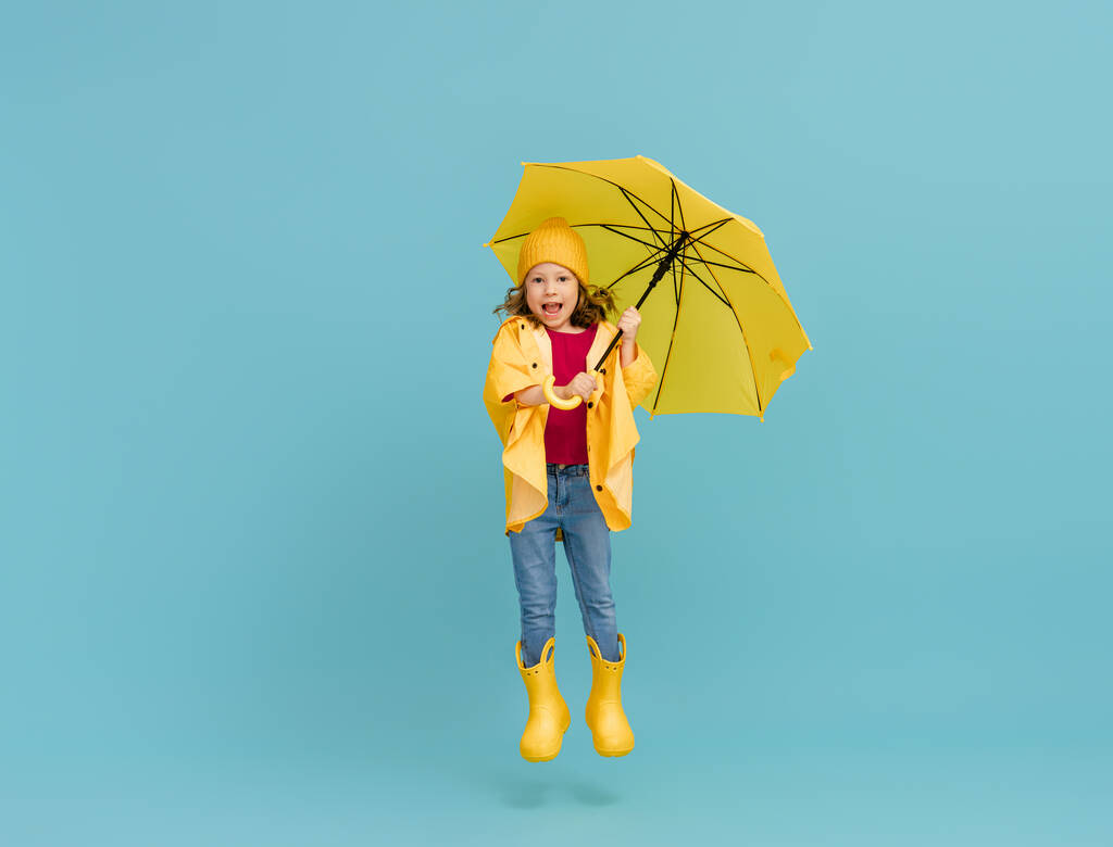 Happy emotional child laughing and jumping. Kid with yellow umbrella on colored teal background. - Photo, Image