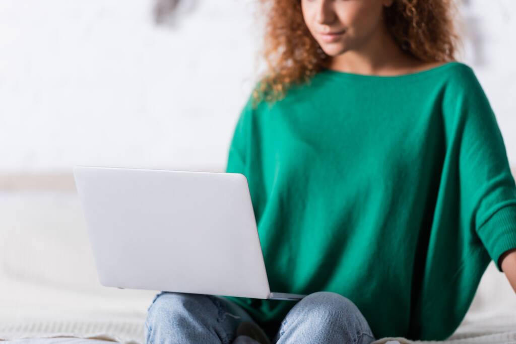 Selective focus of young woman using laptop in bedroom  - Photo, Image