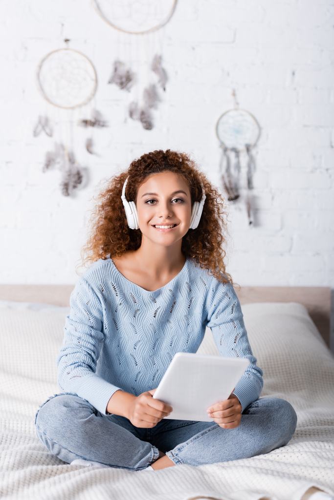 Selektywne skupienie kobiety w swetrze słuchanie muzyki w słuchawkach i trzymanie tabletu cyfrowego w sypialni  - Zdjęcie, obraz