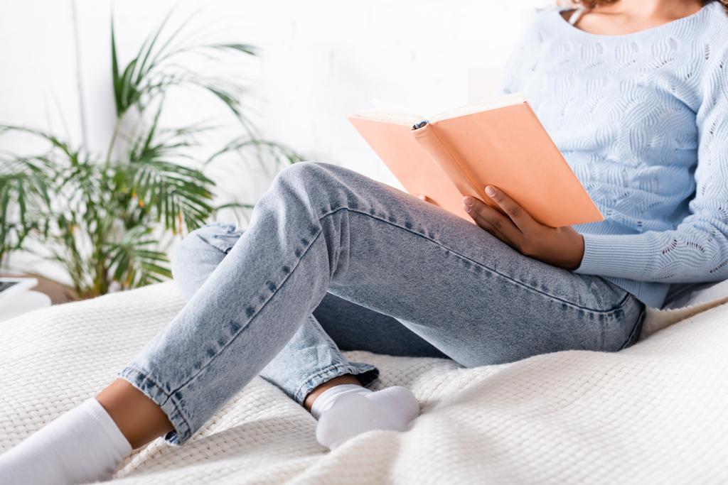 Vista ritagliata di donna in jeans e calzini lettura libro sul letto  - Foto, immagini