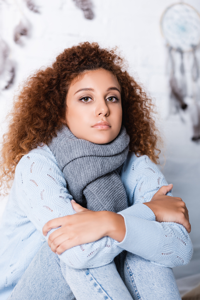 Red haired woman in scarf and sweater looking at camera at home  - Photo, Image