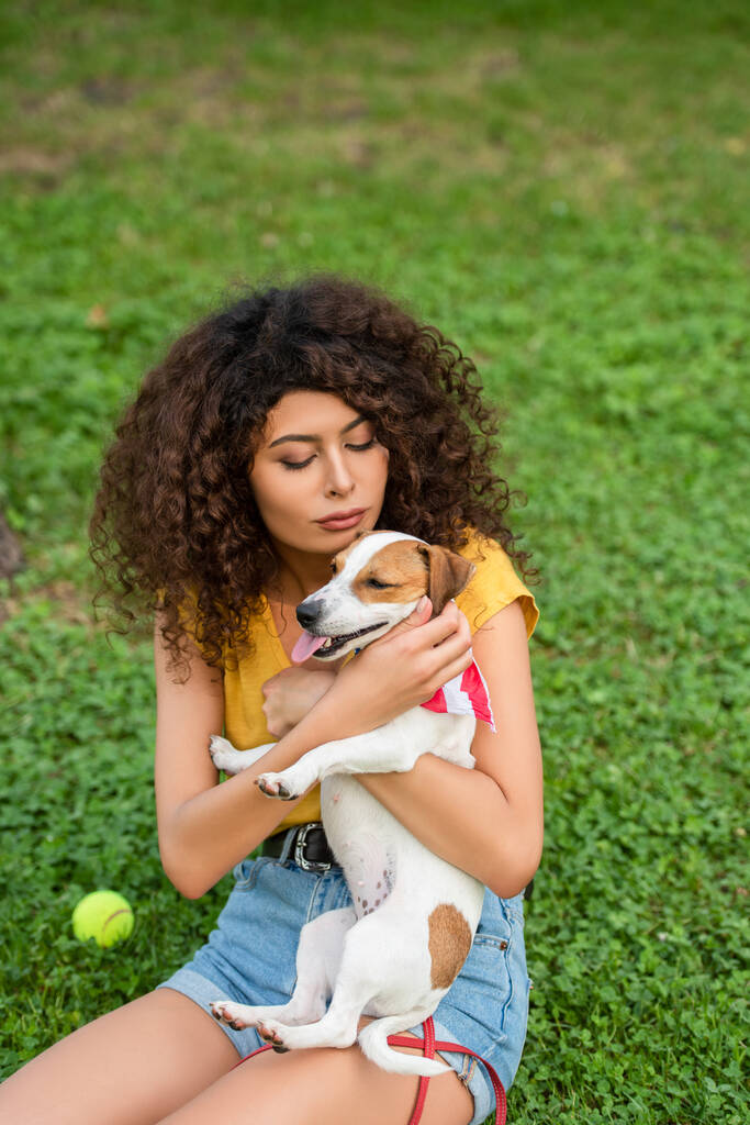 Selektivní zaměření mladé ženy sedící a držící psa na trávě - Fotografie, Obrázek