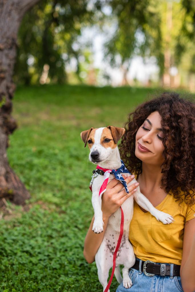 Foco seletivo de jovem segurando cão vestindo bandana bandeira americana - Foto, Imagem