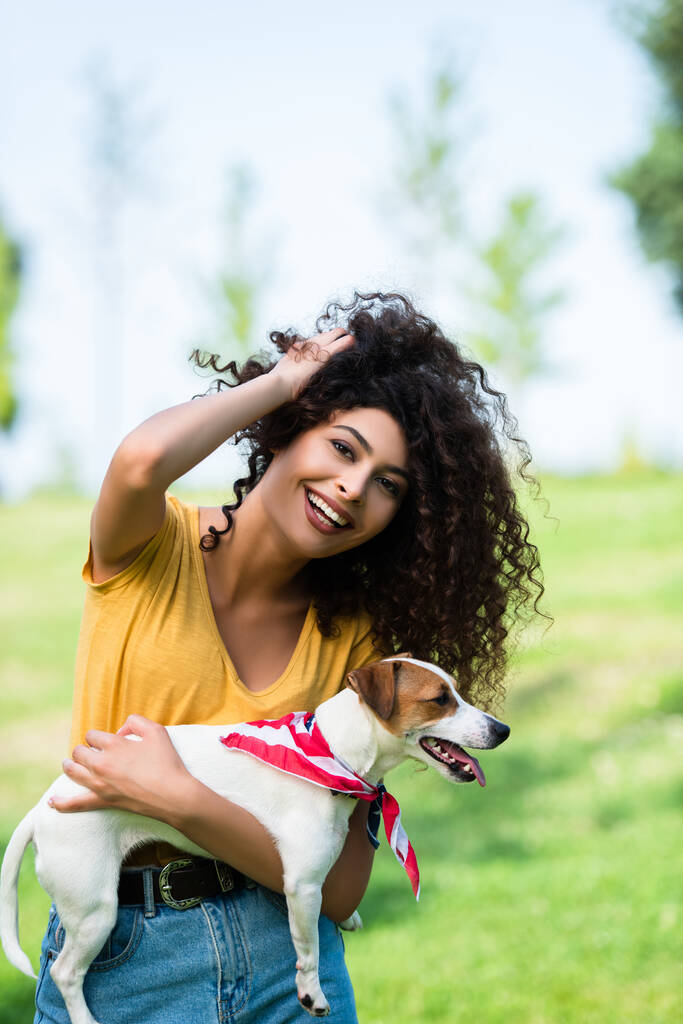 joyeuse, brune femme touchant les cheveux bouclés tout en tenant Jack Russell Terrier chien - Photo, image