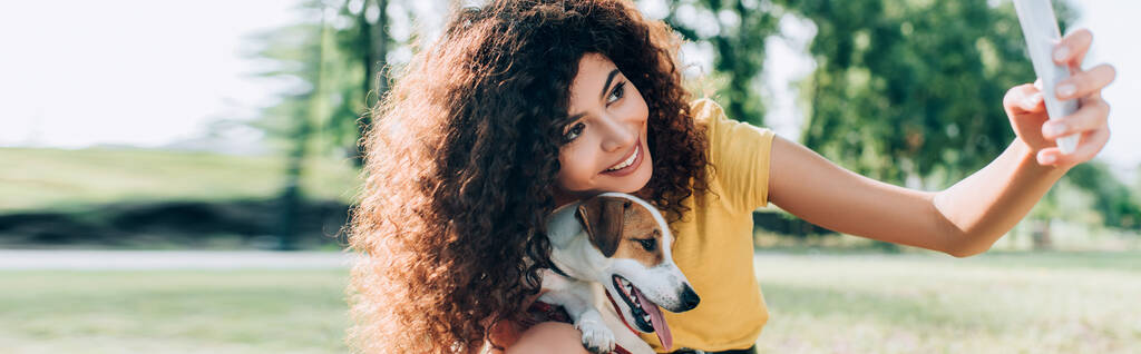 panoramic crop of curly woman taking selfie on smartphone with jack russell terrier dog - Photo, Image