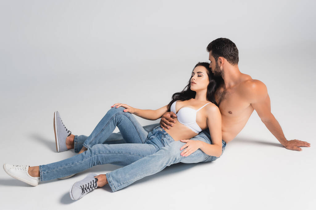 hombre sin camisa en jeans y mujer en sujetador acostado en gris - Foto, imagen