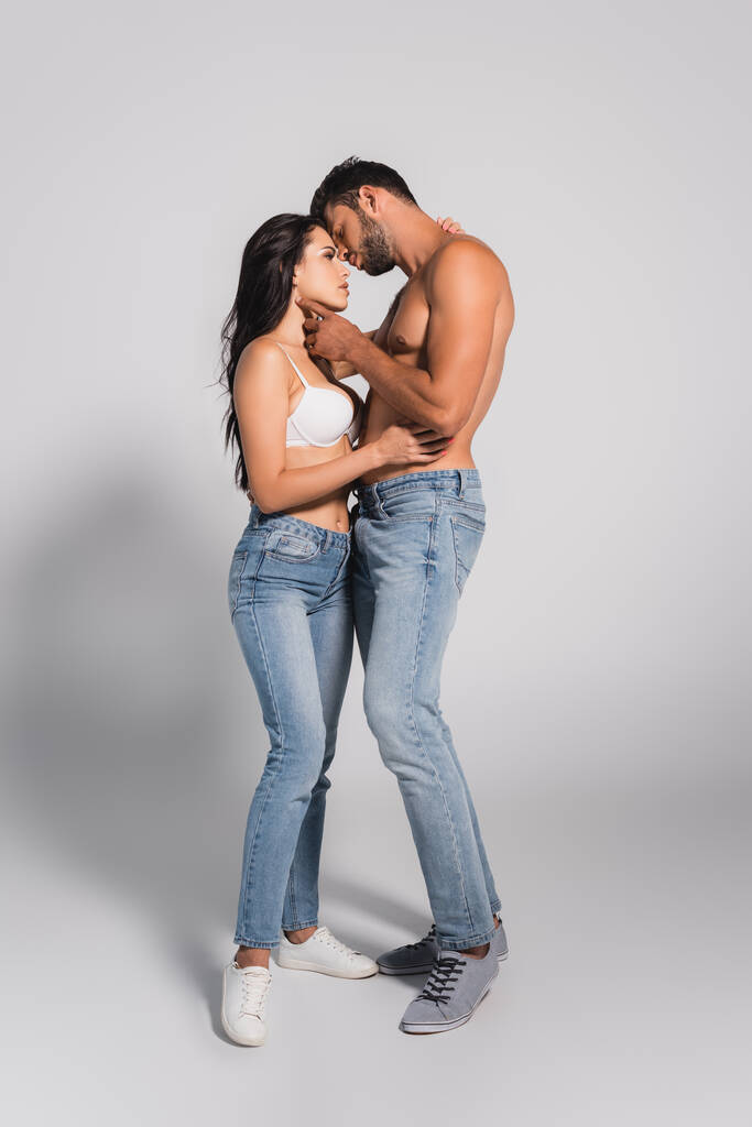 homem muscular de pé e tocando mulher sedutora no sutiã em cinza - Foto, Imagem