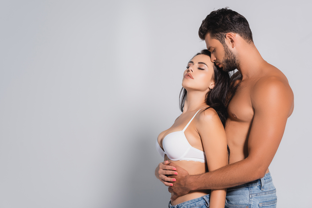 homem muscular de pé e abraçando mulher sedutora no sutiã em cinza - Foto, Imagem